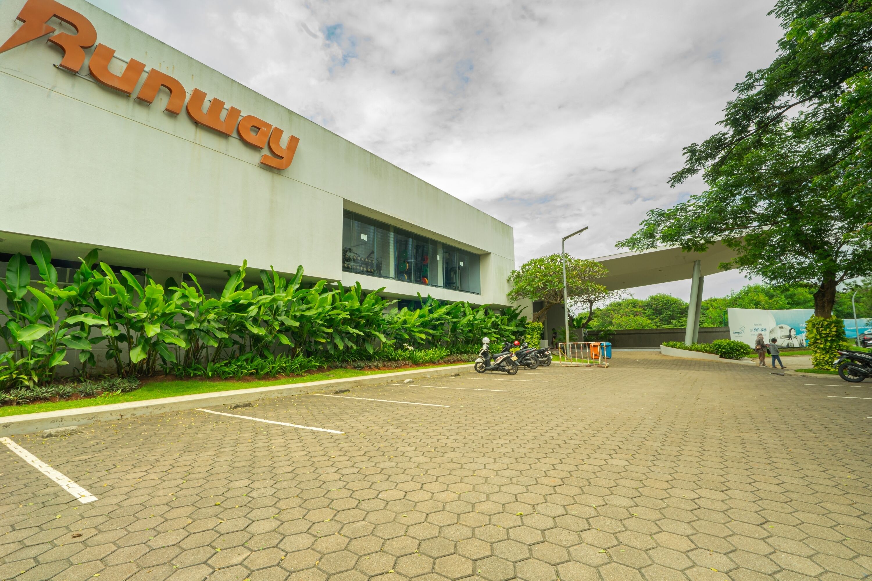 A Runway building with a paved entrance, a motorcycle parked in front, and a person walking.