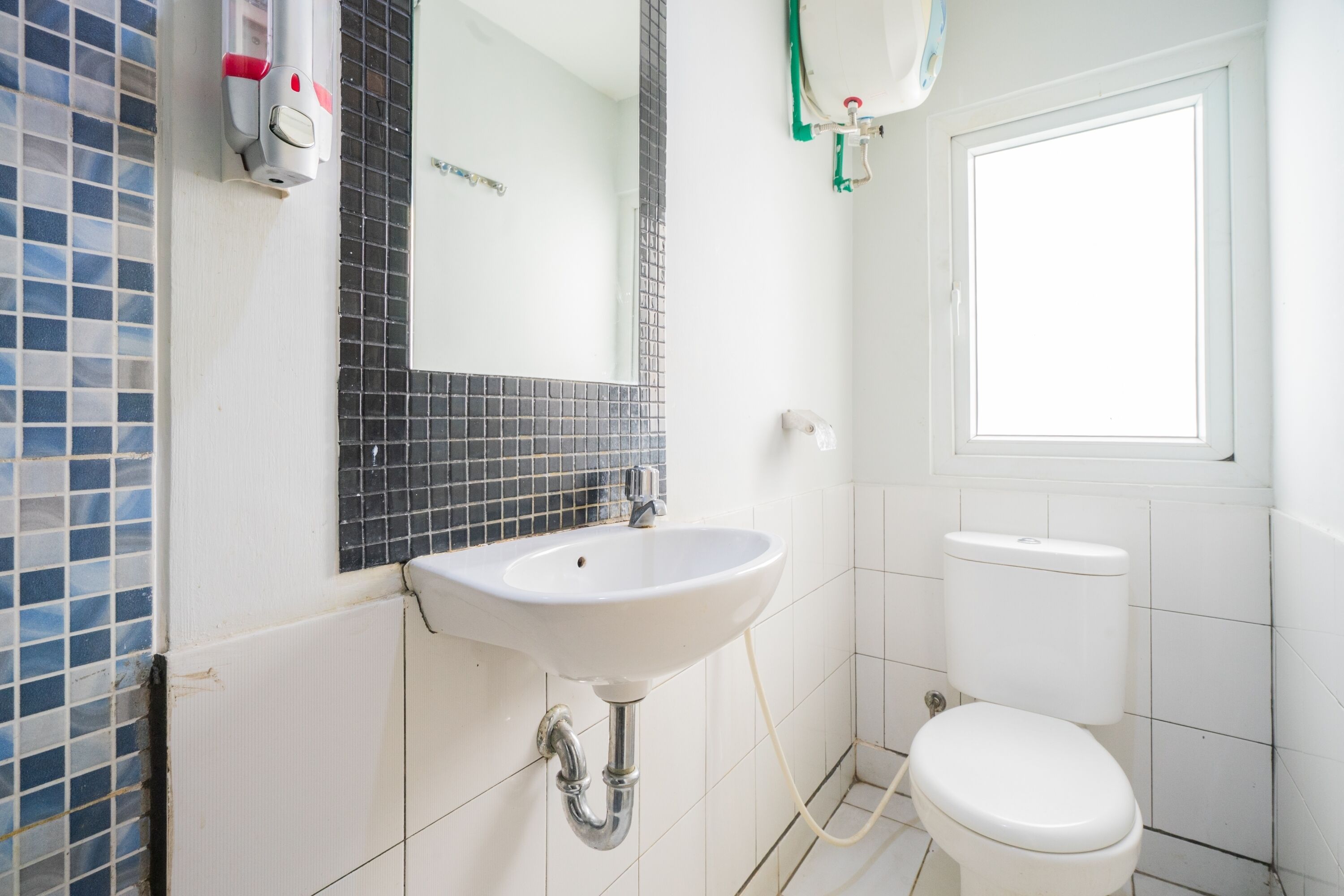 A bathroom with a white sink, a mirror, a toilet, and a window.