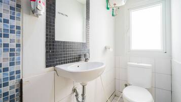 A bathroom with a white sink, a mirror, a toilet, and a window.