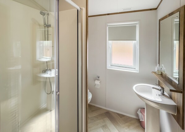 A modern bathroom with a glass shower enclosure, a sink with a wooden vanity, and a window providing natural light.