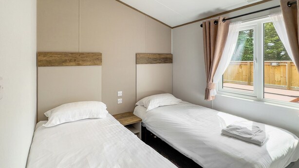 Ein Zimmer mit zwei Betten, einem Vorhangfenster, einem hölzernen Kopfteil und einem kleinen Nachttisch.