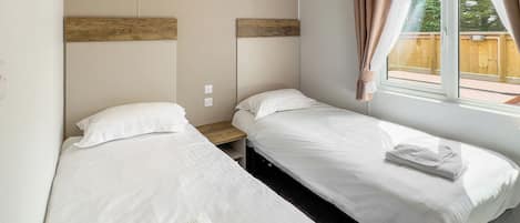 A room with two beds, a window with curtains, a wooden headboard, and a small wooden nightstand.