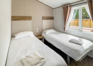 A room with two beds, a window with curtains, a wooden headboard, and a small wooden nightstand.