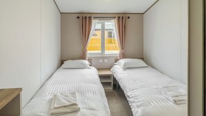 Ein Zimmer mit zwei Einzelbetten, einem Vorhangfenster, einer Holzbank und Blick auf ein gelbes Gebäude.
