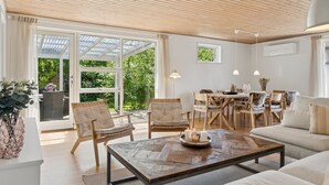 Amplia sala de estar con techo de madera, ventanas grandes y una acogedora disposición de asientos que incluye un sofá y sillones.