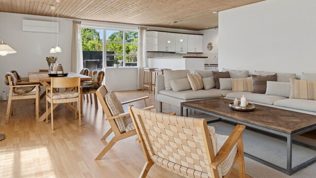 Un amplio espacio de estar con techo de madera, una mesa de comedor con sillas, un conjunto de sofás y una mesa de centro.
