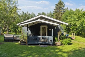 A small wooden cabin with a porch, surrounded by greenery.