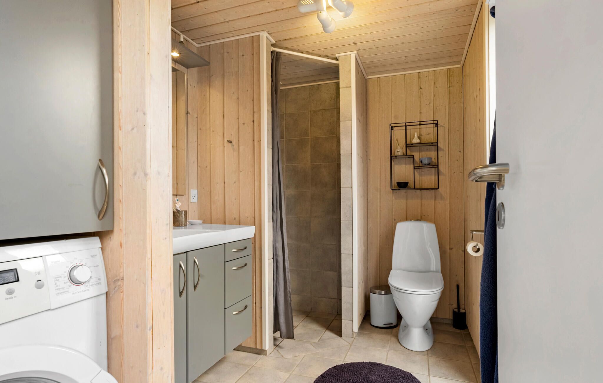 A compact bathroom with a washing machine, grey cabinets, a toilet, and a shower area.