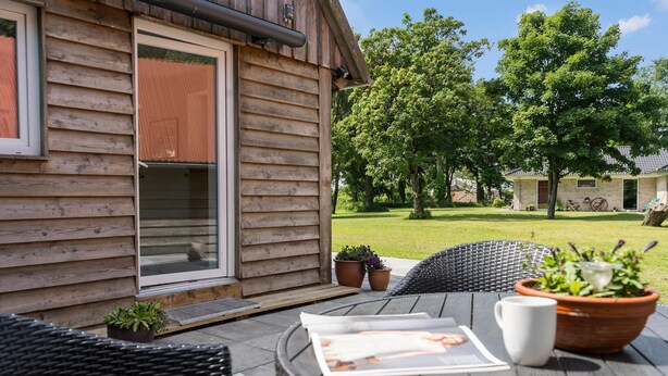 Eine Holzhütte mit einer Schiebeglastür, einer Terrasse mit Korbmöbeln und Topfpflanzen.