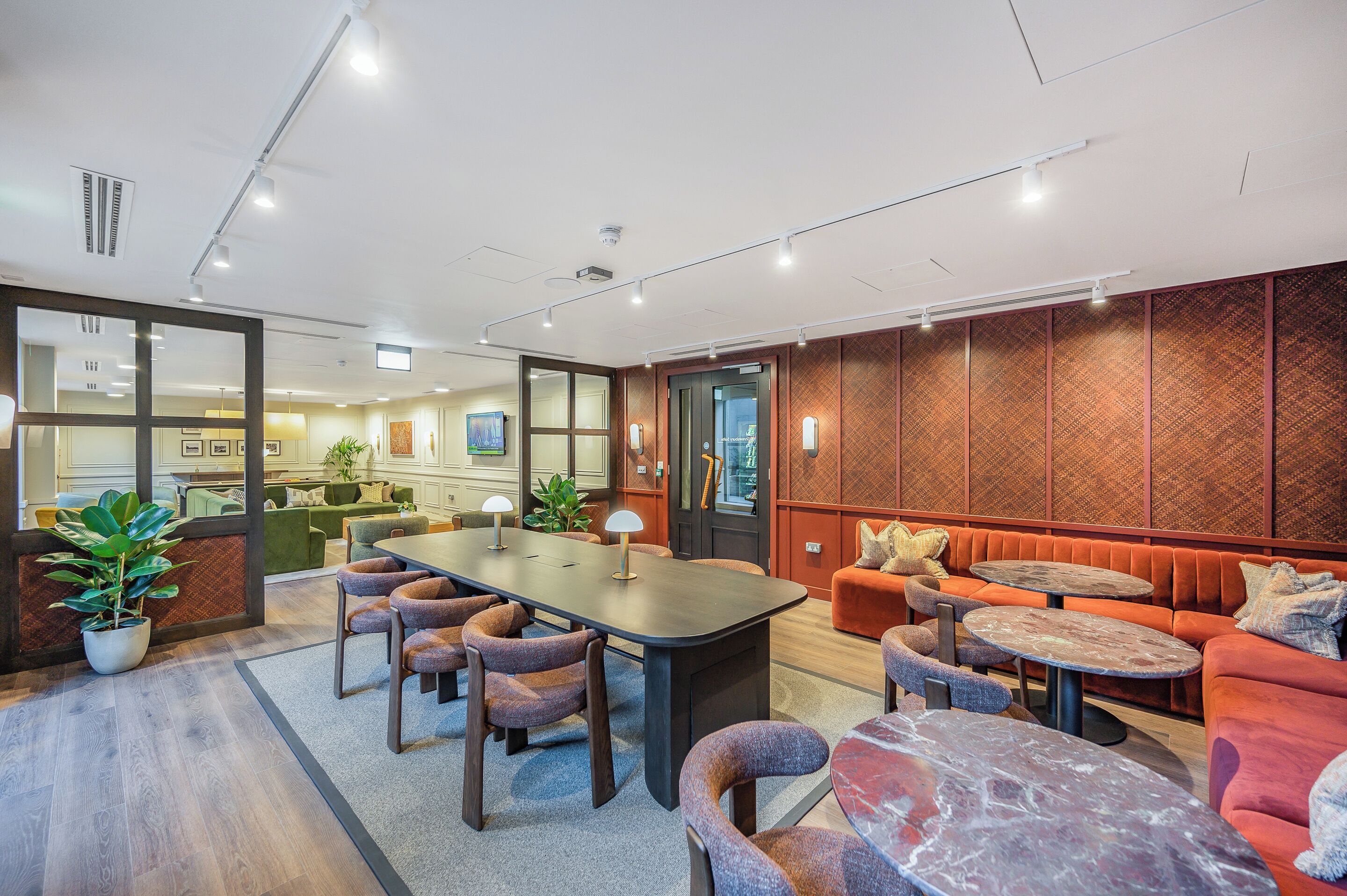 A modern conference room with a long table, comfortable seating, and a view into a kitchen area.