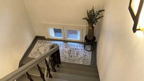 Un escalier orné d’un tapis à motifs, une plante en pot et une fenêtre donnant sur un mur de briques.