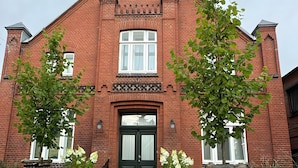 Un bâtiment en briques rouges, doté d’une façade symétrique, d’une entrée centrale avec des portes à double battant et d’une petite fenêtre circulaire au-dessus de la porte.