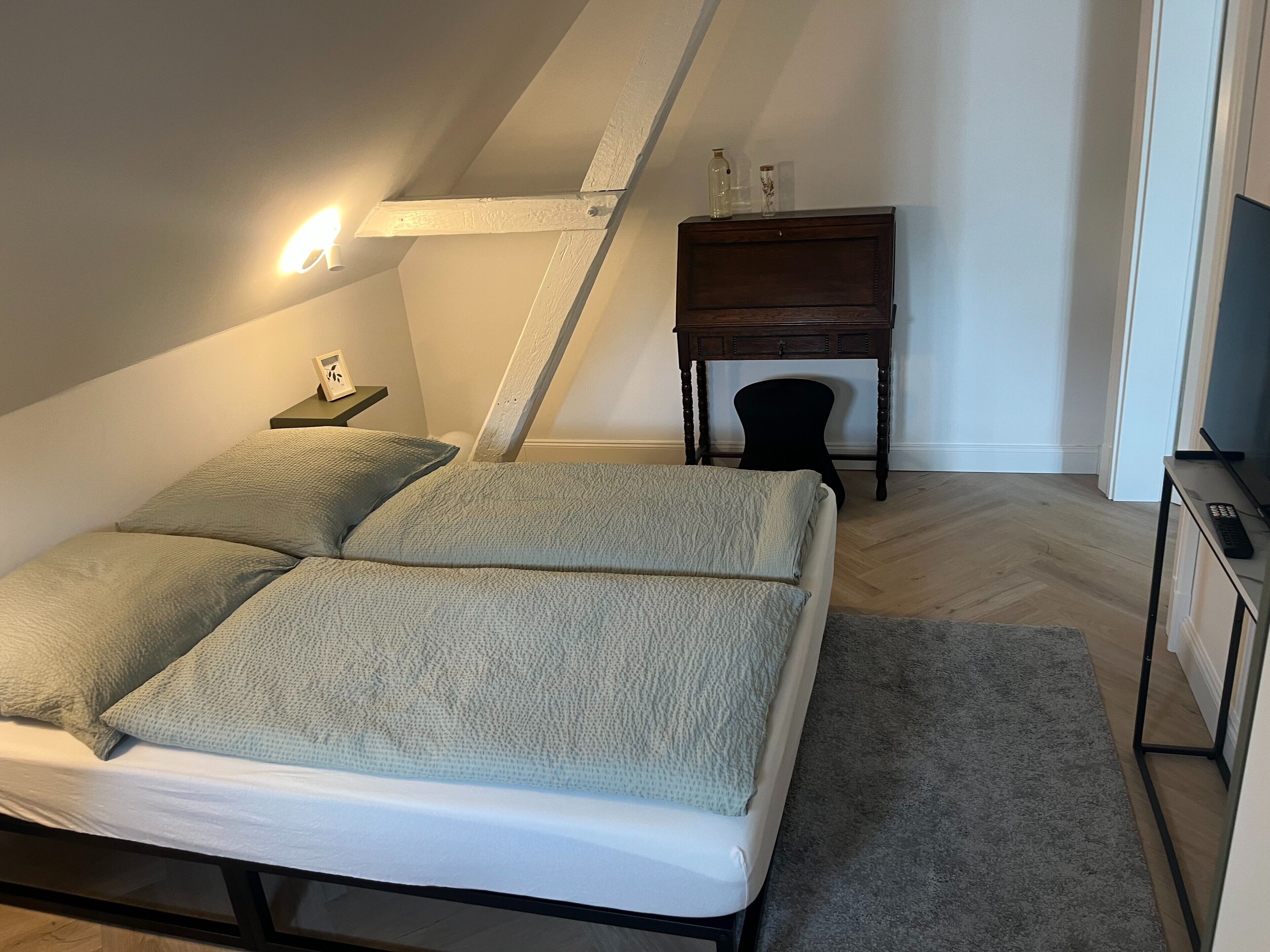 Ein Schlafzimmer mit Bett, Nachttisch, Lampe und einem kleinen Holzkasten.