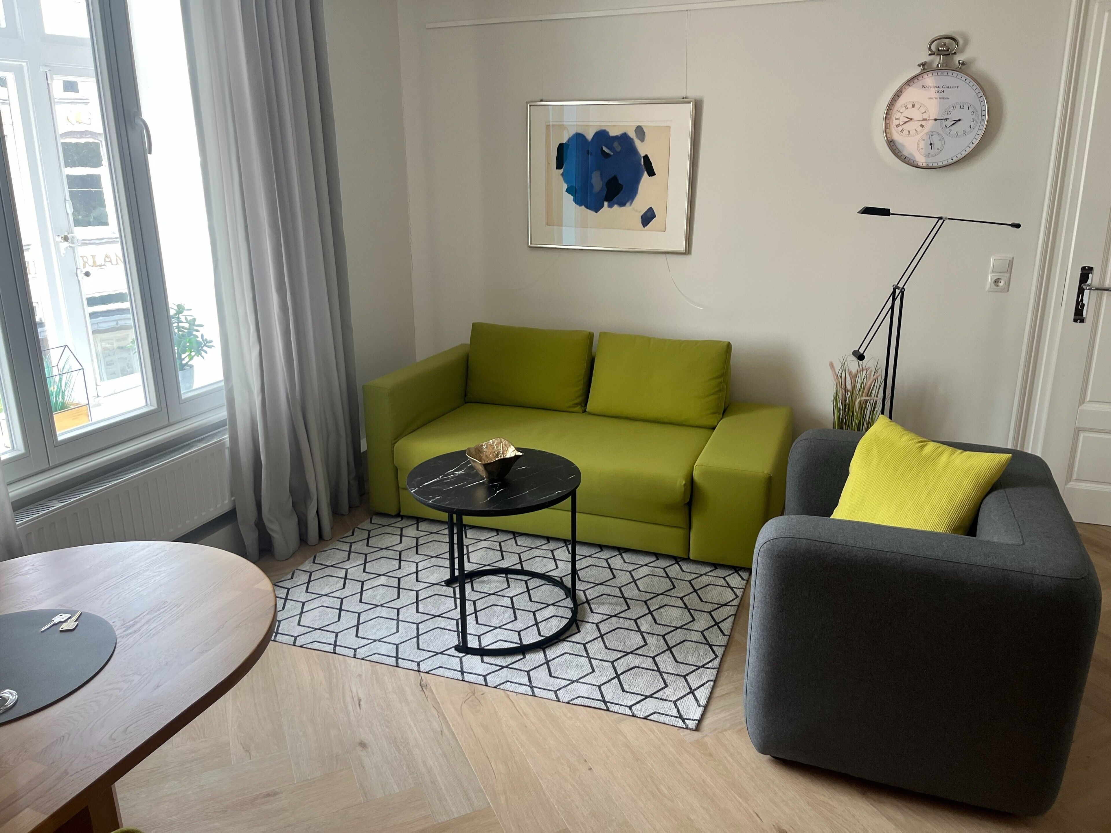 A living room with a green sofa, a gray armchair, a small black table, and a geometric patterned rug.
