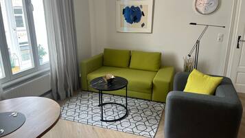 A living room with a green sofa, a gray armchair, a small black table, and a geometric patterned rug.