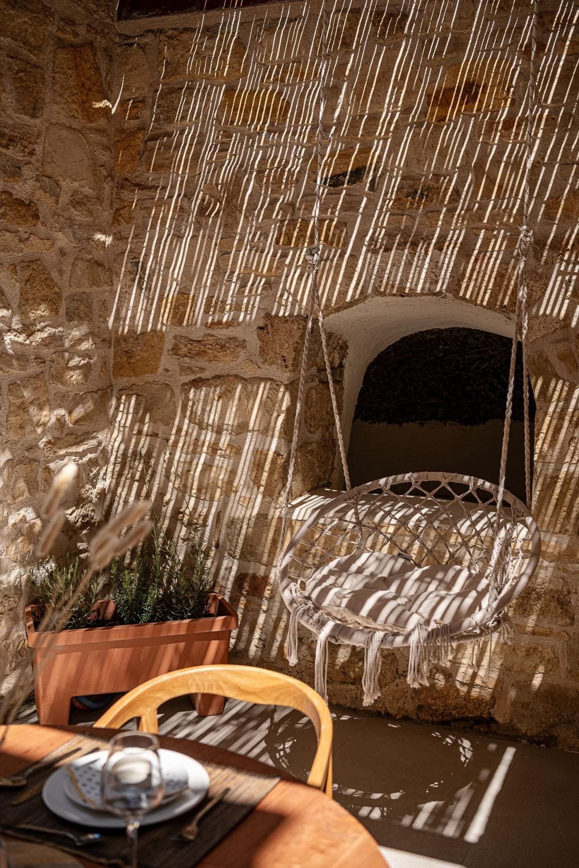 A stone-walled room with a hanging chair and a table set for dining.