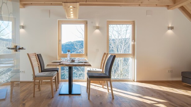 Ein Essbereich mit Tisch, Stühlen und großen Fenstern mit Blick auf Bäume und Berge.
