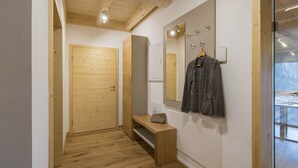 Ein Flur mit Holzboden, einer Bank, einem Kleiderhaken mit einer Jacke und einer Tür.