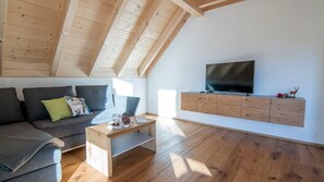 A modern living room with a sloped ceiling, a sofa, a coffee table, a TV, and a wooden cabinet.