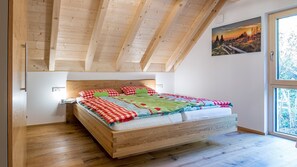 A bedroom with a wooden bed, a nightstand, a window with a view, and a wooden ceiling.