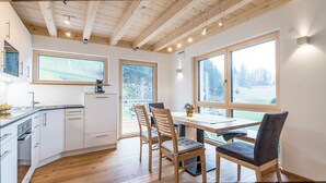 A modern kitchen with wooden cabinets, a dining area with a table and chairs, and large windows offering views of the outdoors. - Apartment 'Dollenberg' with Mountain View, Balcony and Wi-Fi (Bad Peterstal-Griesbach)