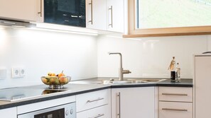 A modern kitchen with white cabinets, a stainless steel sink, and a bowl of fruit on the counter.