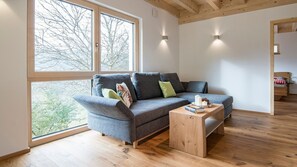 A modern living room with a grey sofa, a wooden coffee table, and a large window with a view of trees.