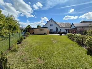 A house with a large lawn, a wooden deck, and a fenced garden area.