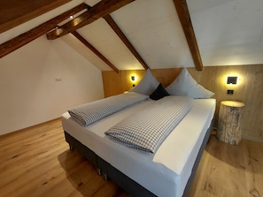 A bedroom with a wooden ceiling, a bed with checkered bedding, two wall-mounted lights, and a wooden nightstand.