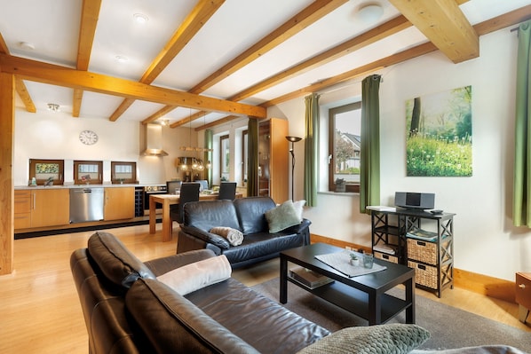 A spacious living area with a sofa, coffee table, and a dining table. A kitchen with modern appliances is visible in the background.