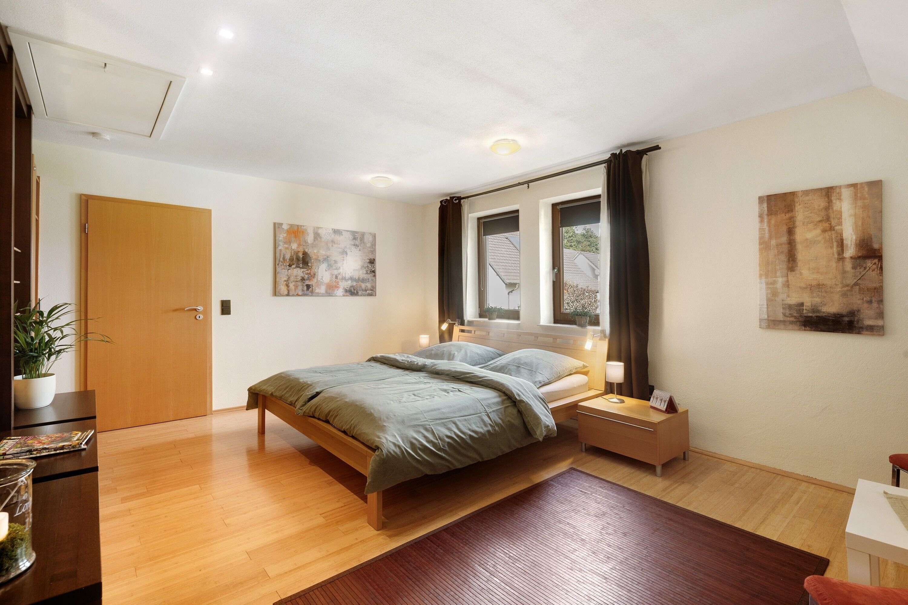 Ein Schlafzimmer mit Bett, Nachttischen, einem Fenster mit Vorhängen, einer Tür und einem Bild an der Wand.