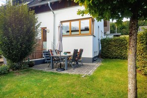 A house with a patio, a dining table, chairs, and a potted plant.