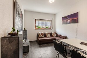 Une pièce moderne comprenant un canapé, une table à manger, des chaises, une fenêtre donnant sur un paysage urbain et un tableau accroché au mur.