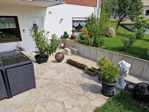 Une terrasse avec un sol en pierre, des plantes en pot, du mobilier d’extérieur et un mur blanc portant le numéro 35.