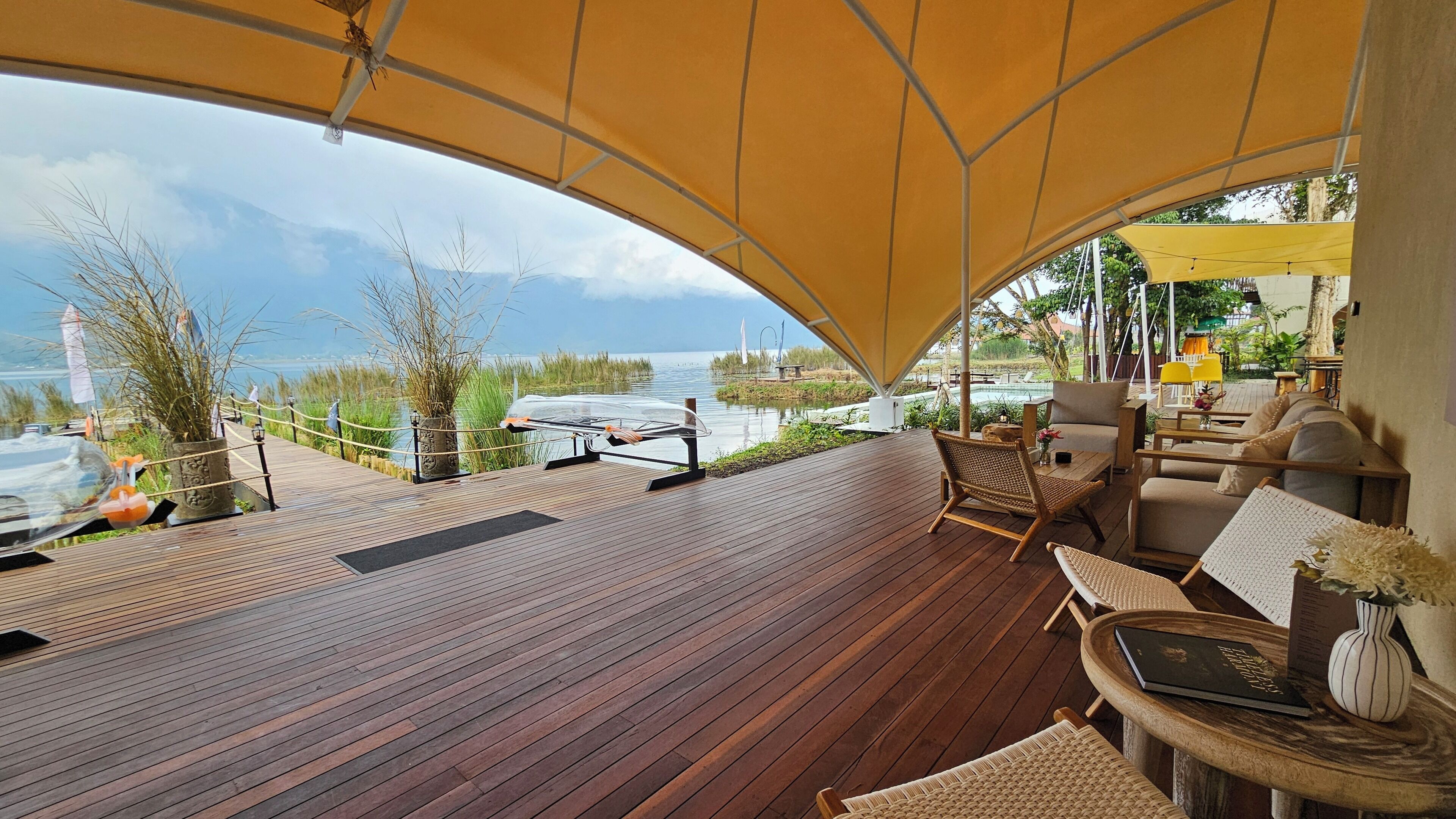 Een houten terras met buitenmeubilair, een zonnescherm en uitzicht op een wateroppervlak.