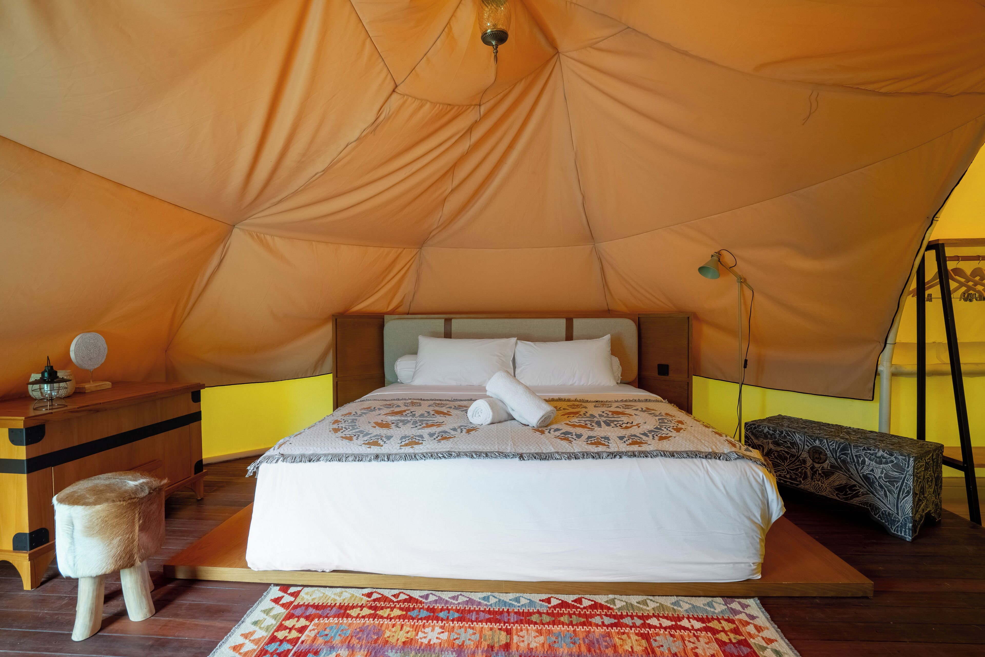A tented room with a bed, bedside table, lamp, and a small stool.