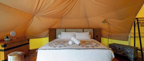 A tented room with a bed, bedside table, lamp, and a small stool.