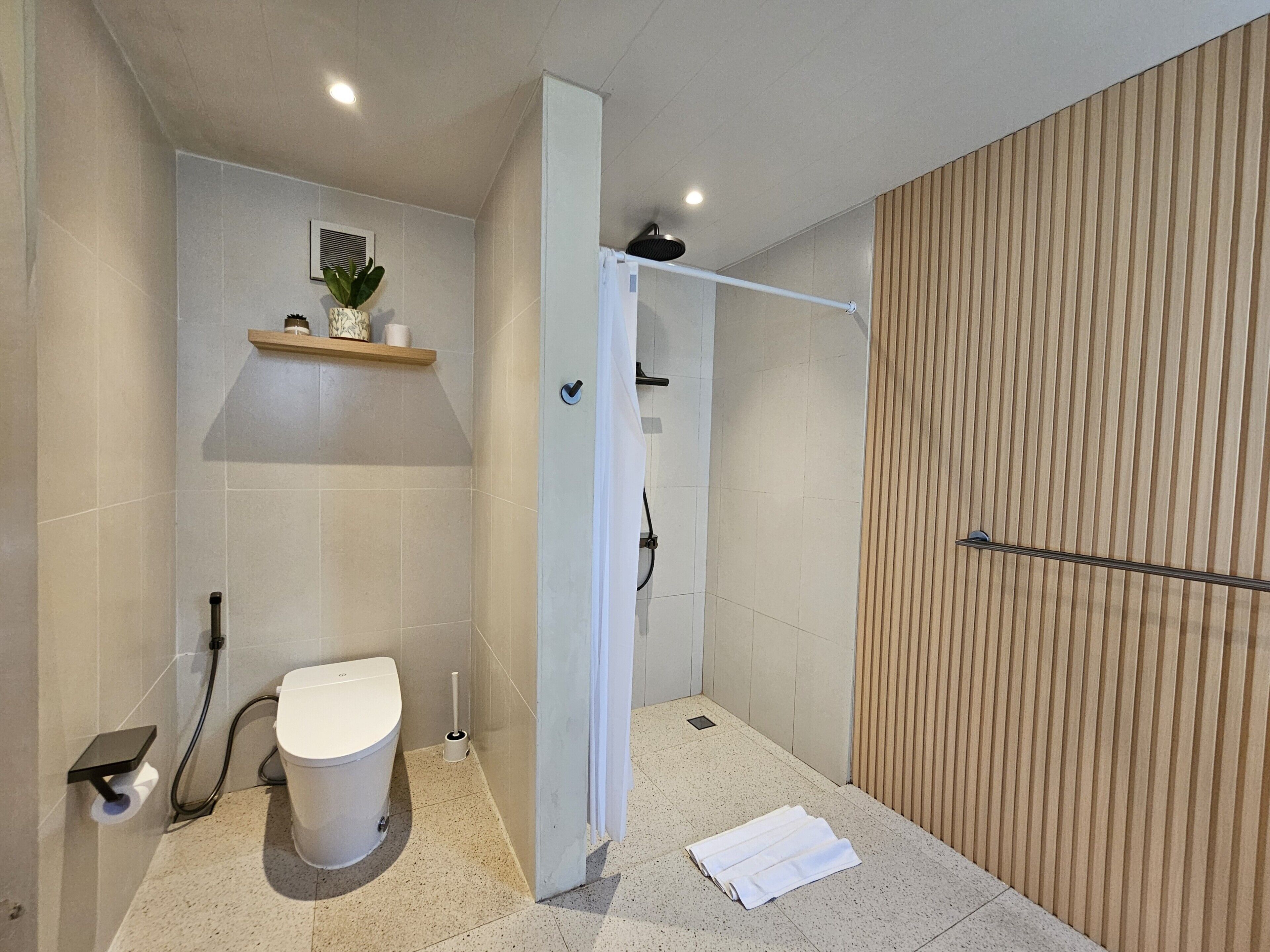 A modern bathroom with a toilet, shower, and a towel on the floor.