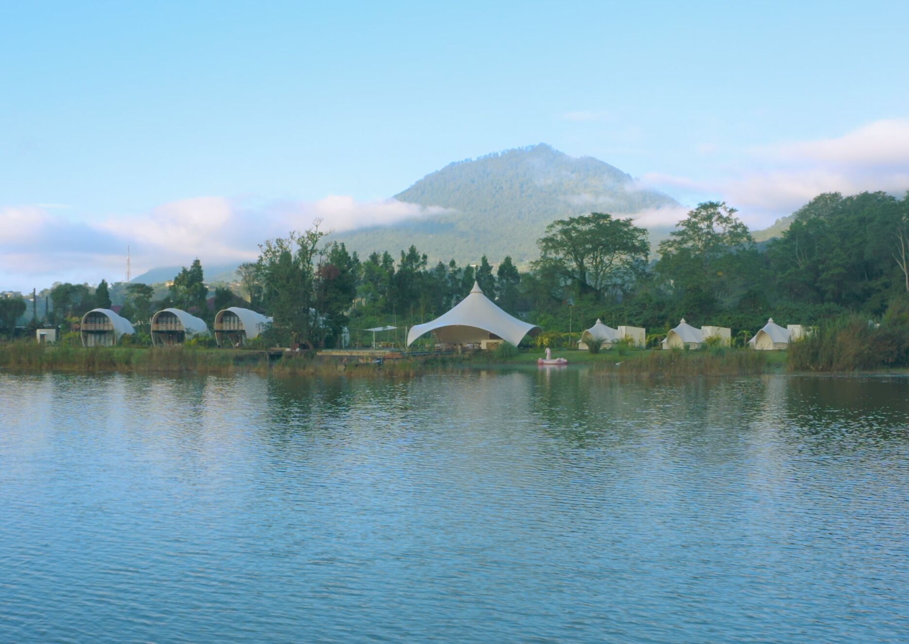 A lakeside view with several dome-shaped huts and a large white tent.