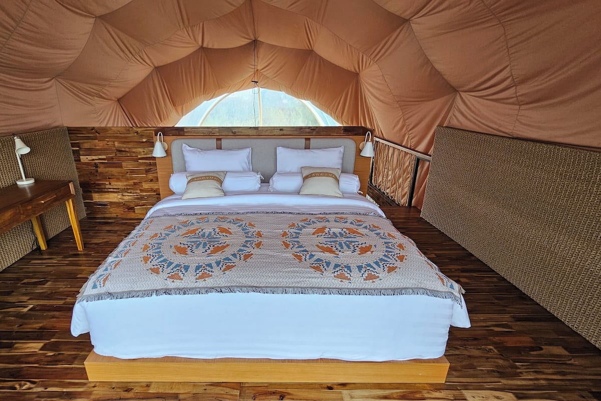 A cozy tented room with a wooden bed, a desk, and a lamp.