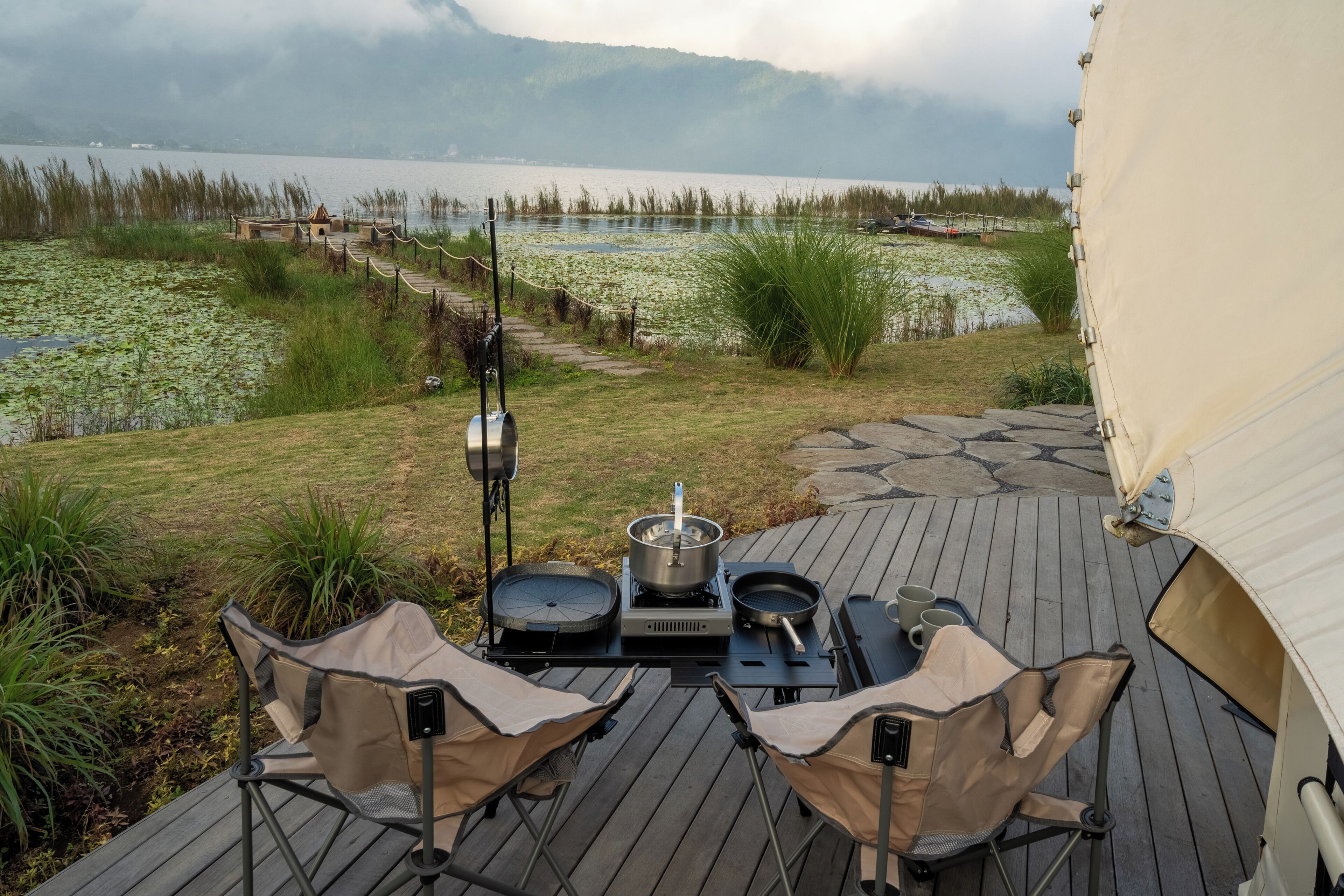 A deck with camping equipment, including a portable stove, chairs, and a tent.