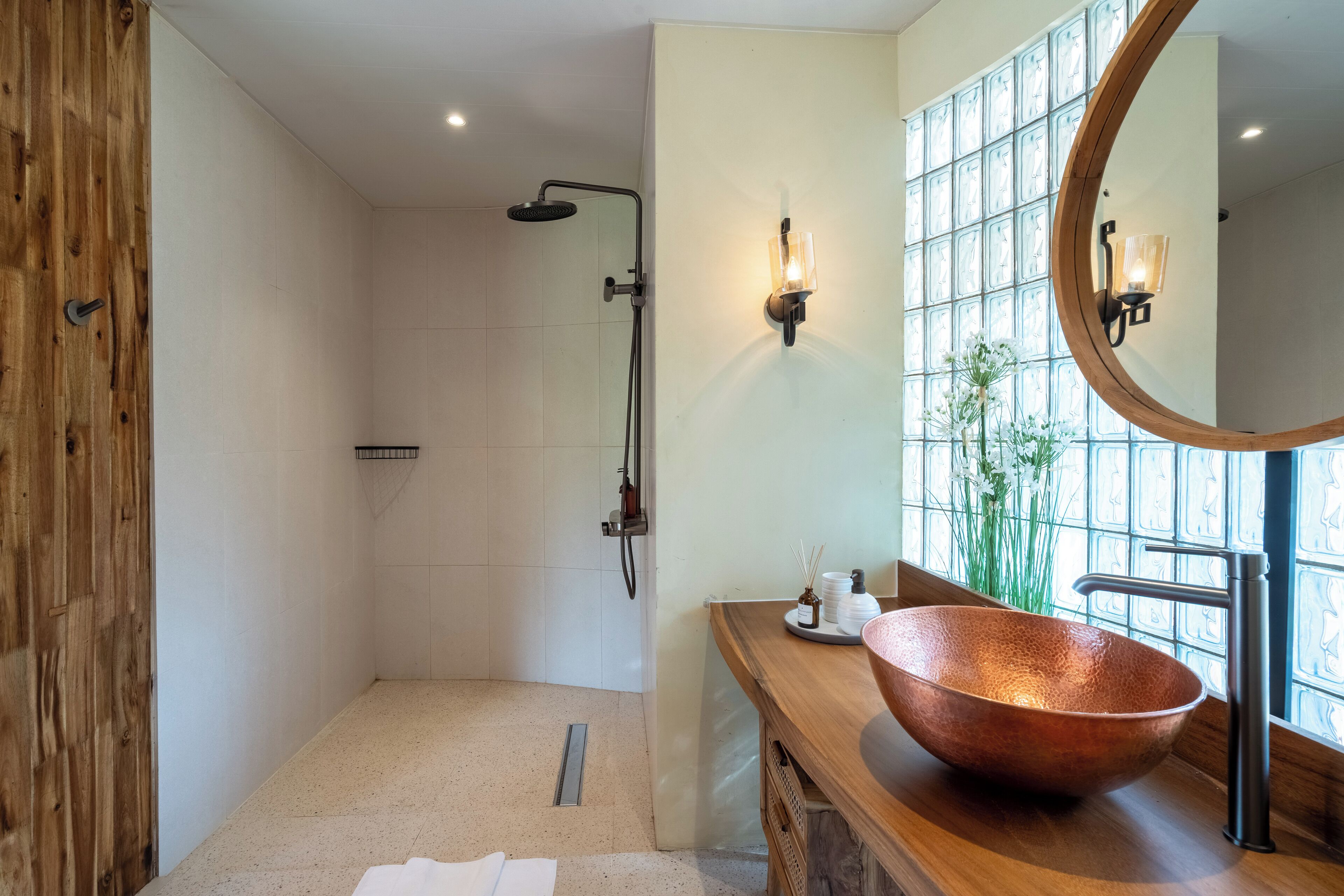 A modern bathroom with a wooden vanity, a copper sink, a glass shower enclosure, and a large mirror.