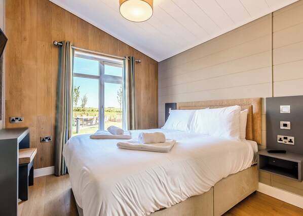 Une chambre moderne avec un grand lit, des murs en bois, une vue sur l’extérieur et une table de chevet avec une lampe.