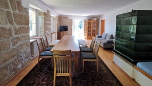 Uma sala de estar ampla com uma mesa de jantar de madeira, cadeiras, um sofá e uma televisão.
