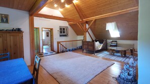 Um quarto espaçoso no sótão, com teto de madeira, uma cama grande, uma mesa de jantar e vista para o quarto vizinho.