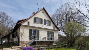 Uma casa de dois andares com varanda, rodeada por um jardim com flores amarelas.