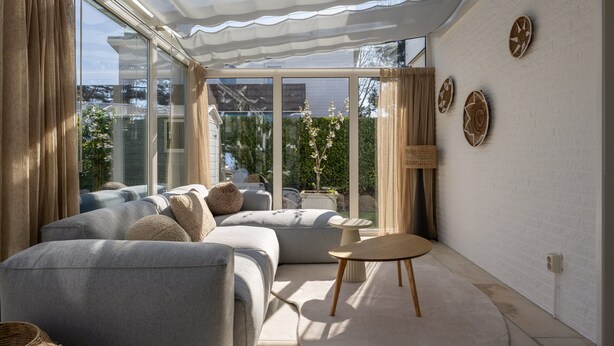 Ein modernes Wohnzimmer mit einer grauen Sofagarnitur, einem runden Couchtisch und Blick durch große Fenster.