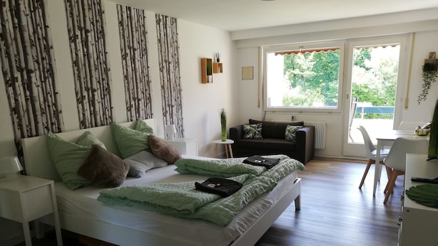 A modern bedroom with a bed, a small table, a sofa, and a window with a view of greenery. - Apartment 'Lived-in' with Mountain View, Balcony and Wi-Fi (Bad Urach)