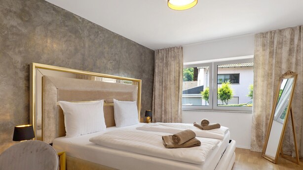 A hotel room with a large bed, a bedside table with a lamp, a chair, and a window with curtains. - Apartment 'Ferienwohnung' with Private Terrace, Private Garden and Wi-Fi (Sinsheim)