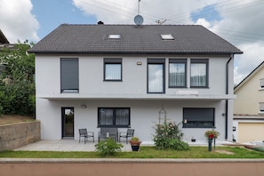 Et toetagers hus med tegltag, parabolantenne og en lille have med plantede krukker.